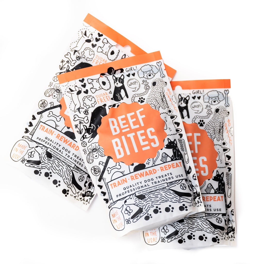 Multiple HoodHound Beef Bites dog treat bags arranged in a fan layout, showcasing playful illustrated packaging and bright orange branding.